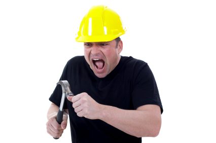 Construction worker grimacing as he hits his thumb with a hammer